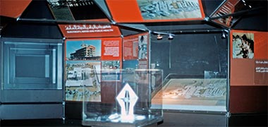 A view of part of the exhibition space with panels, models and a video screen